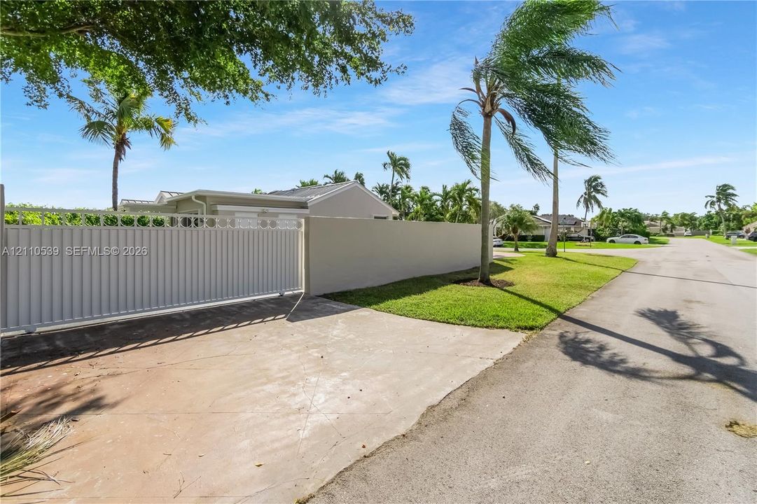 Private gated entrance featuring a solid concrete perimeter wall, metal sliding gate, and mature palm landscaping