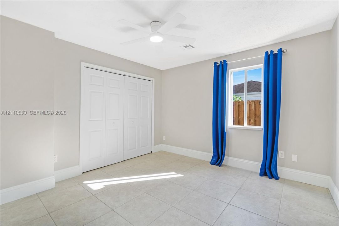 Neutral-toned interior featuring large-format floor tile, a white ceiling fan with integrated lighting, and a double-door closet with paneled detailing