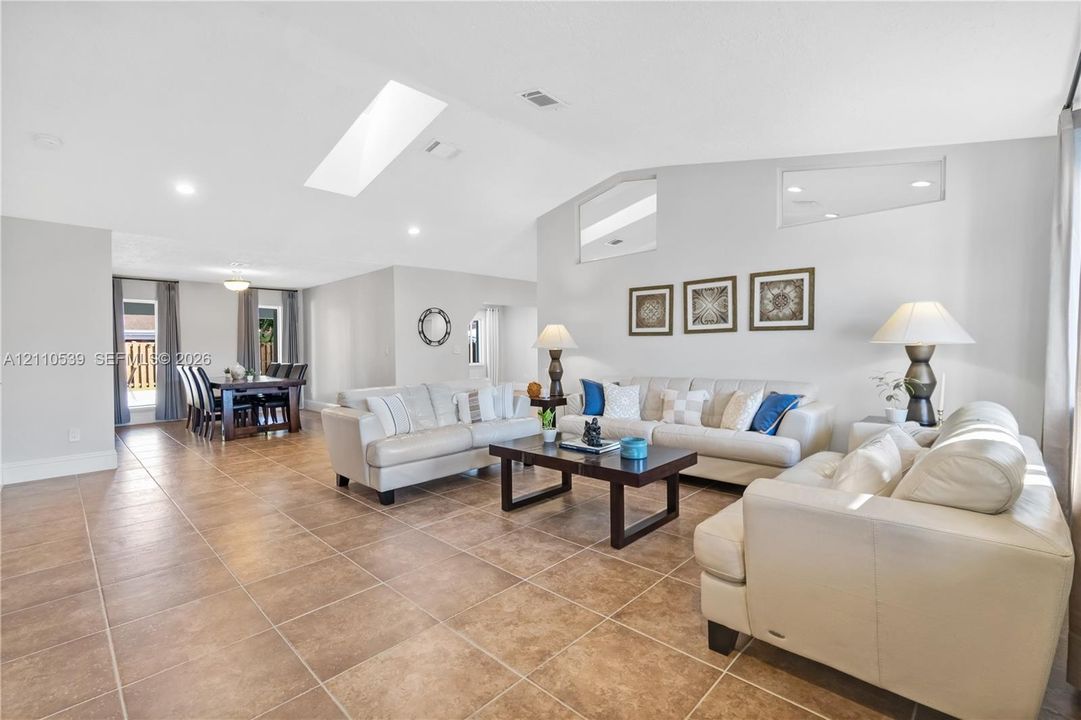 Open-concept living space featuring vaulted ceilings, a large skylight, high-set geometric windows, and tile flooring