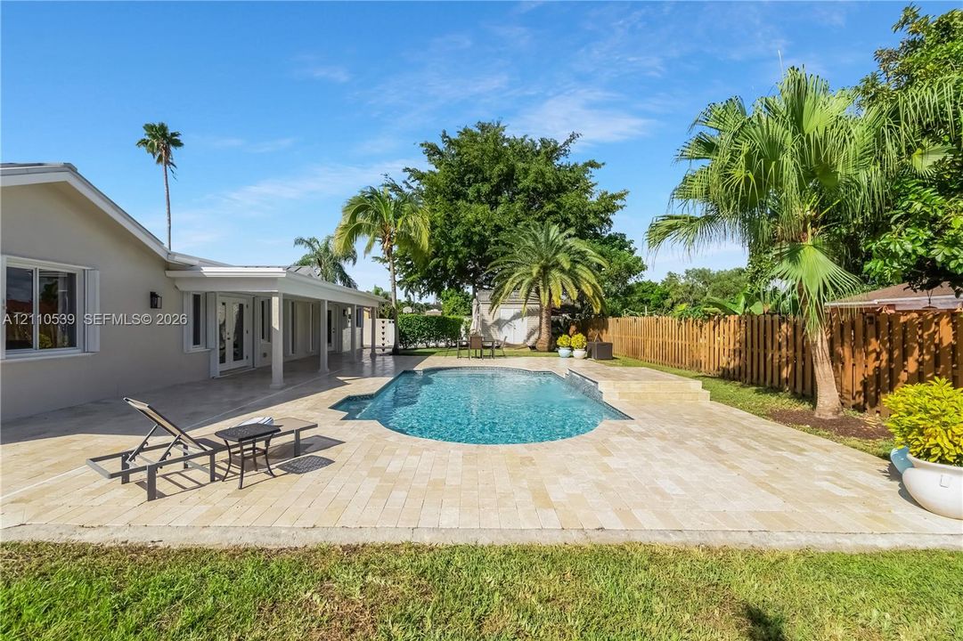 Backyard featuring a paver patio, in-ground swimming pool, covered outdoor living area, wood privacy fencing, and mature palm trees