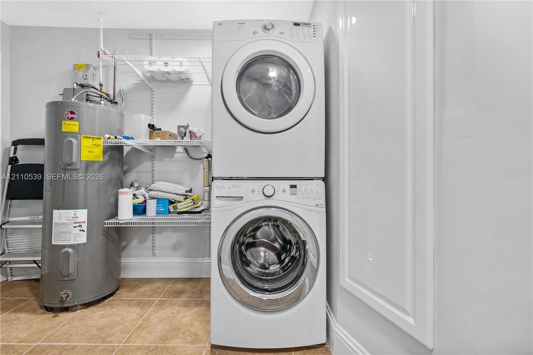 Utility area featuring a stacked washer and dryer, upright water heater, wire shelving system, and ceramic tile flooring
