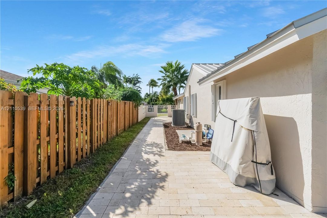 Side exterior featuring a paver stone walkway, vertical wood privacy fencing, and metal roofing