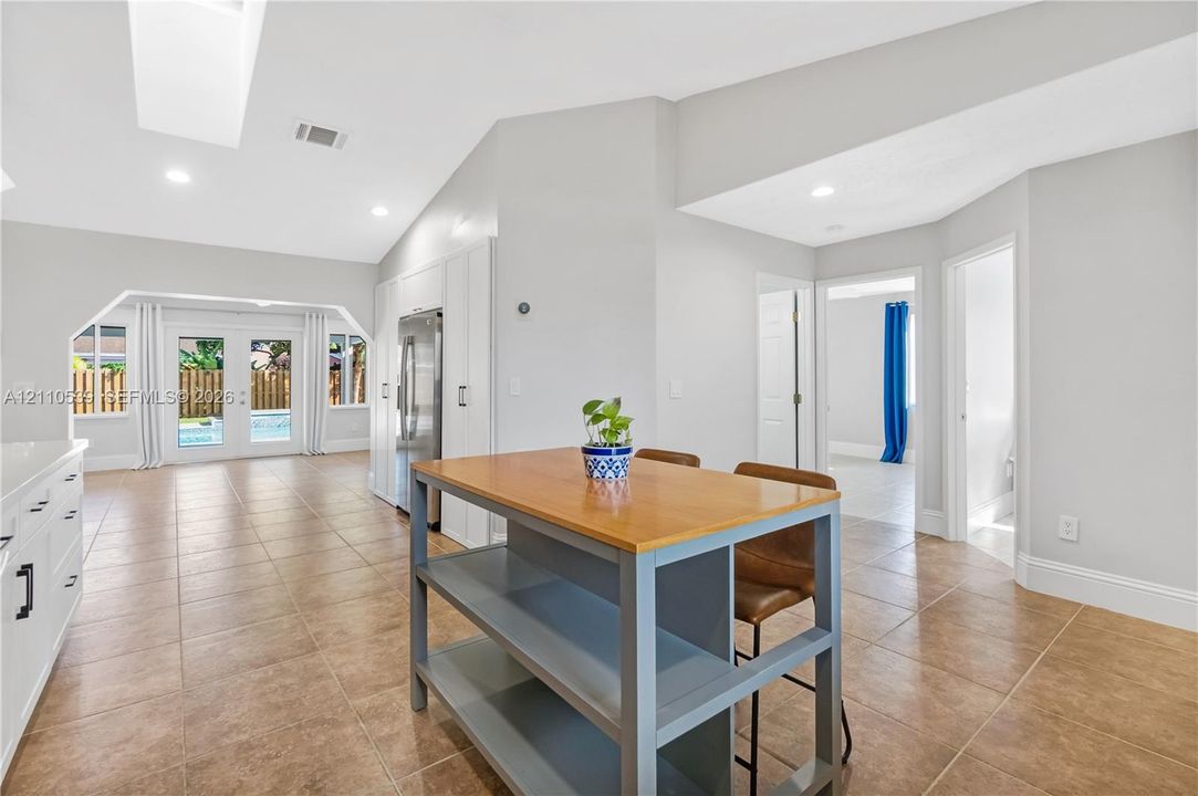 Vaulted ceiling with recessed lighting, neutral tile flooring, white cabinetry, and glass paneled double doors