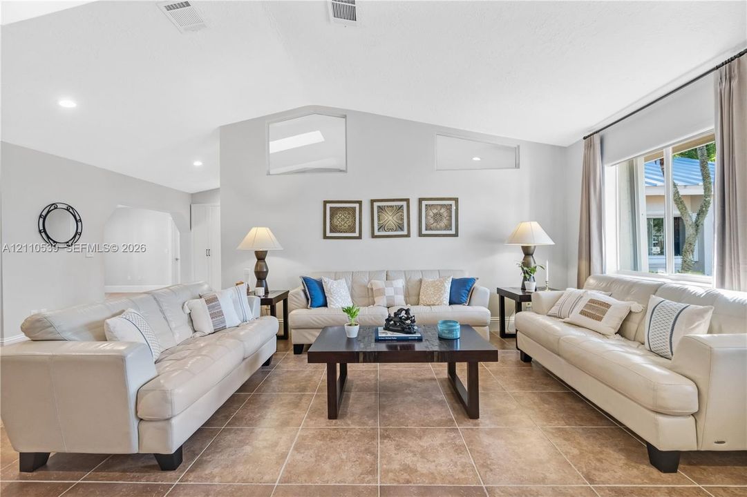Living room featuring vaulted ceilings, oversized tile flooring, recessed lighting, and clerestory windows