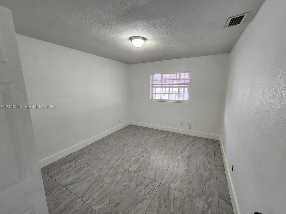 Neutral-toned room featuring large-format tile flooring and a window with security bars