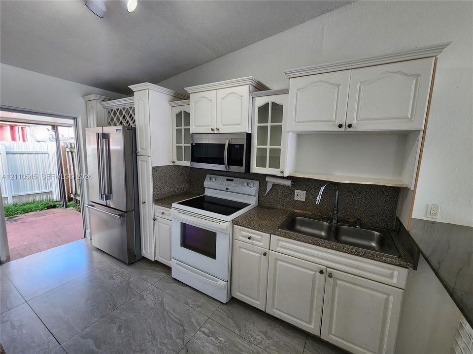 Kitchen featuring white cabinetry with glass-front accents, stone-composite countertops, stainless steel dual-basin sink, built-in wine storage, and large-format tile flooring