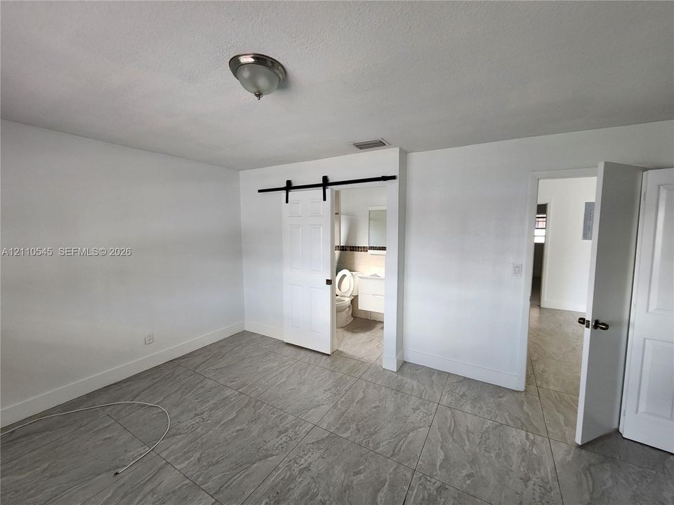 Interior space featuring large-format stone-patterned tile flooring, a white sliding barn door with black hardware, and a semi-flush mount ceiling light fixture
