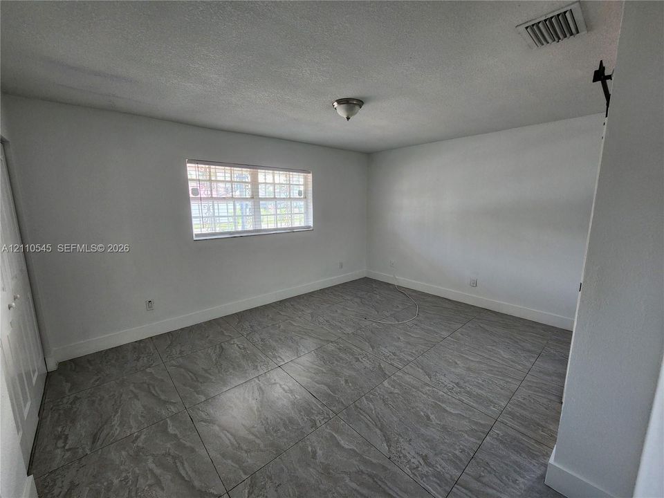 Room featuring large-format tile flooring, textured ceilings, a single window with decorative grids, and a white paneled door