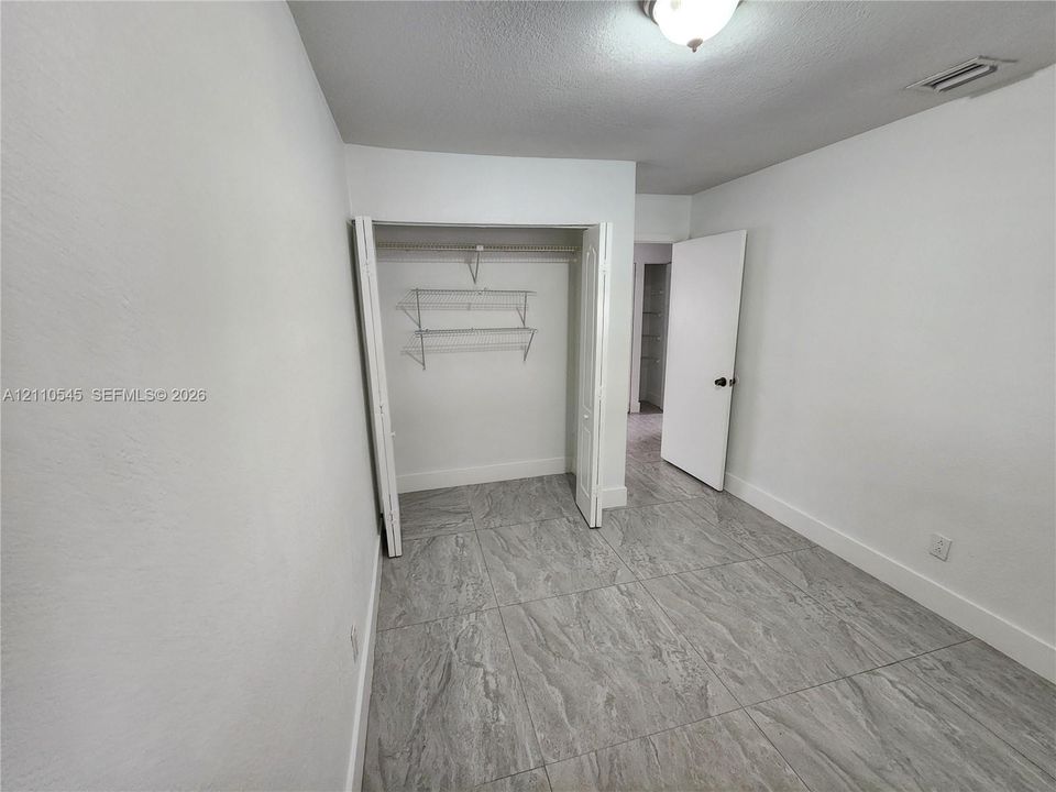 Room featuring large-format tile flooring, a closet with bi-fold doors, white interior walls, and a ceiling-mounted light fixture