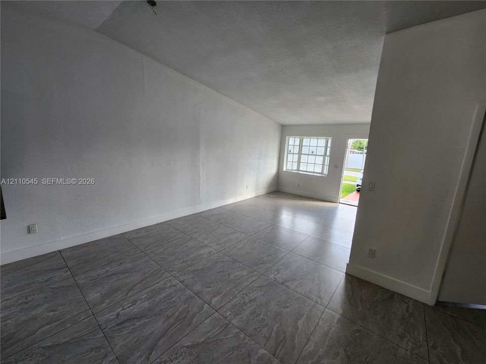 Open-concept room featuring large-format stone-finish tile flooring, white textured walls, and a multi-pane window