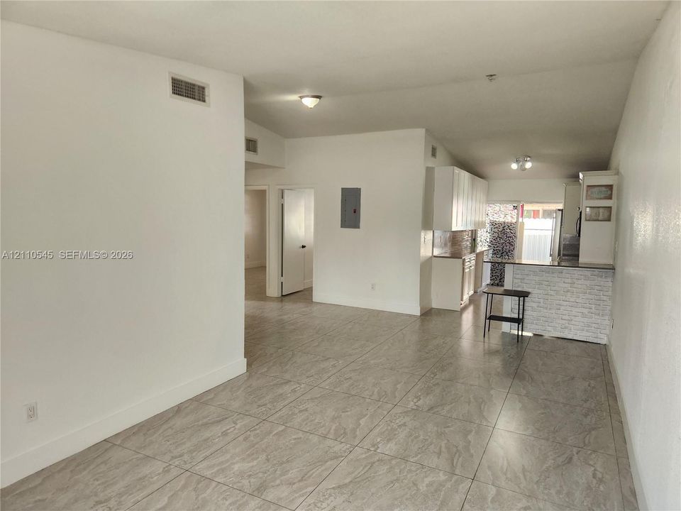 Open-concept area featuring large-format stone-finish tile flooring, kitchen with white cabinetry, textured stone-style backsplash, and a breakfast bar