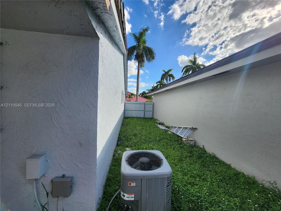 Exterior side yard featuring stucco wall finishes, metal privacy fencing, and an external HVAC unit