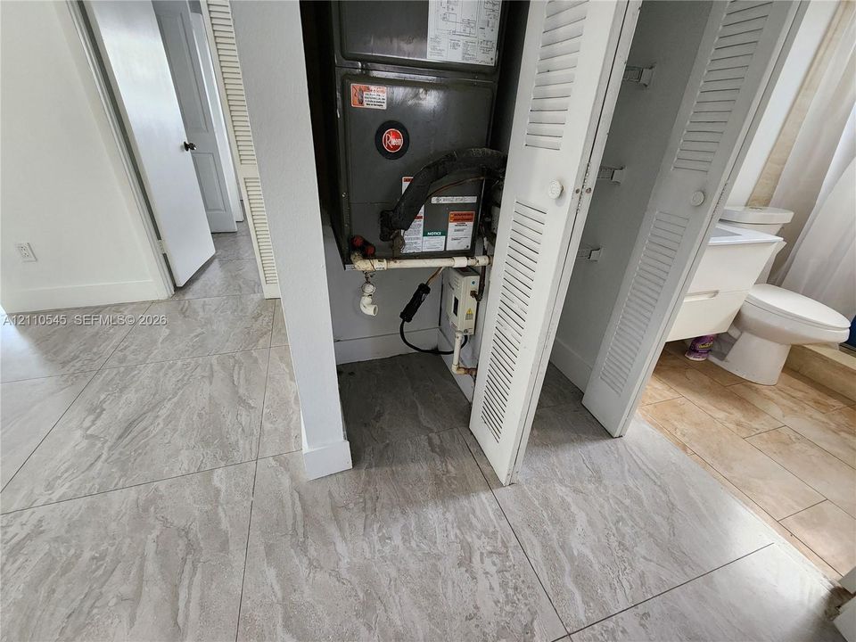 Large-format tile flooring, louvered closet doors, HVAC air handler unit, and a white vanity with integrated sink