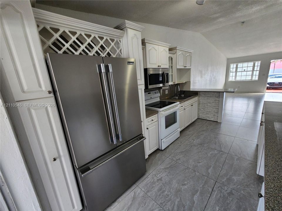 Kitchen featuring white cabinetry with integrated wine rack, stone-finish floor tile, stainless steel refrigerator, microwave, and white range