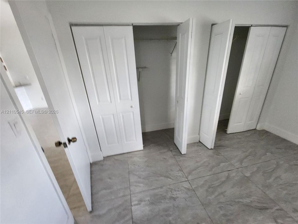 Interior space featuring large-format tile flooring and two sets of white bifold closet doors with built-in shelving and rods