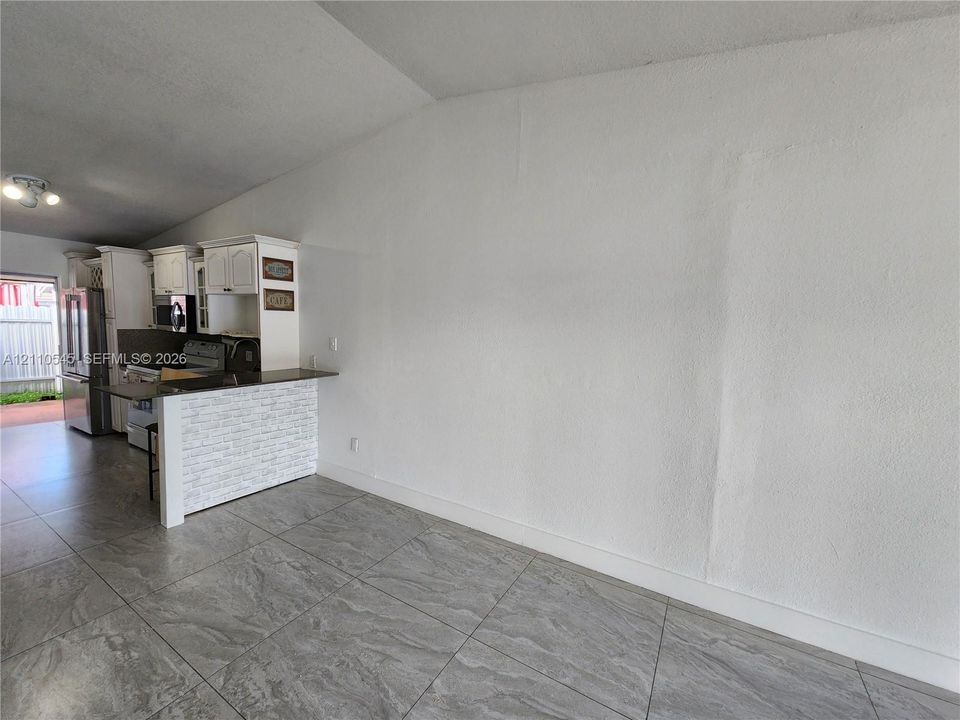 Kitchen featuring large-format tile flooring, a raised breakfast bar with textured stone-veneer facing, dark stone countertops, and white cabinetry