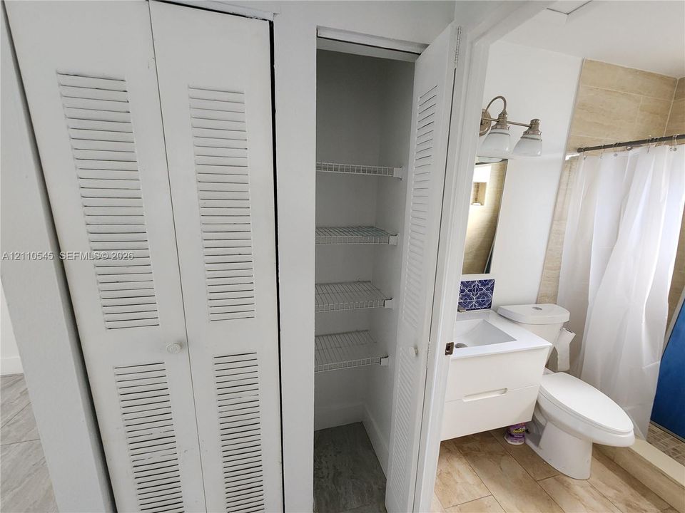 Built-in louvered-door cabinetry featuring integrated wire shelving, a modern floating vanity with a rectangular sink, stone-finish floor tiling, and decorative tile backsplash