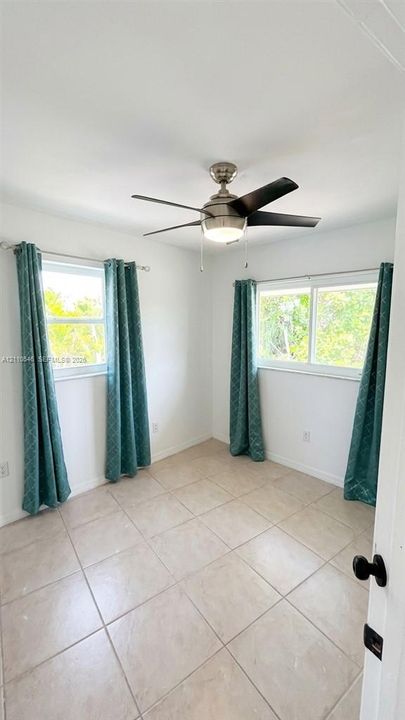 Neutral-toned tile flooring, dual windows, and a ceiling fan with integrated lighting
