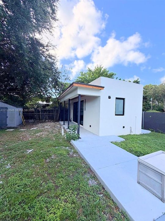 Modern structure featuring a smooth stucco exterior, a covered porch with metal support columns, a concrete walkway, and black-framed windows
