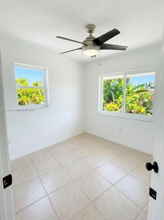 Room featuring large-format ceramic tile flooring, neutral wall finishes, sliding windows, and a multi-blade ceiling fan with integrated lighting