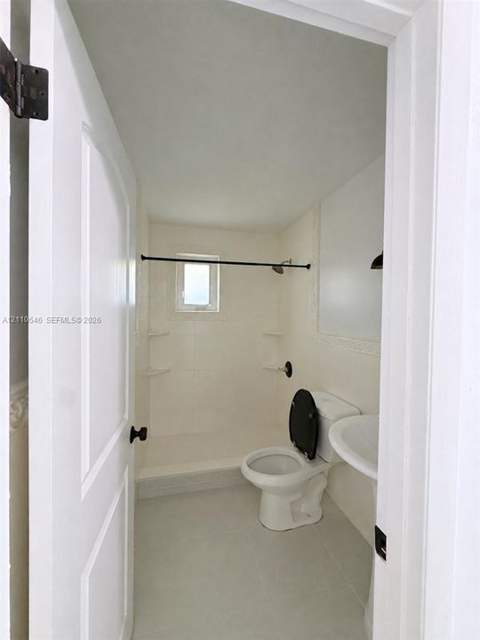 Bathroom featuring a tub-shower combination with integrated shelving, white pedestal sink, tiled flooring, and matte black hardware fixtures