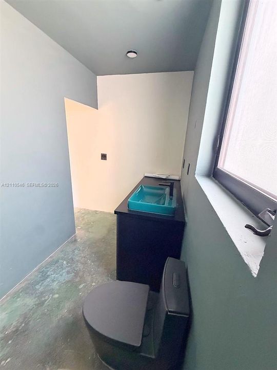Bathroom featuring a dark-toned vanity cabinet, a colored vessel sink, a matte-finish faucet, and a dual-flush toilet