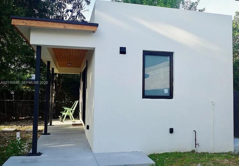 Modern minimalist exterior featuring smooth stucco siding, a covered porch with wood-finished ceiling panels, dark metal structural supports, and black-framed windows