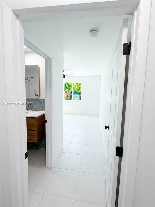 White tile flooring, wood-finish vanity with a white rectangular countertop sink, geometric backsplash tile, and matte black hardware