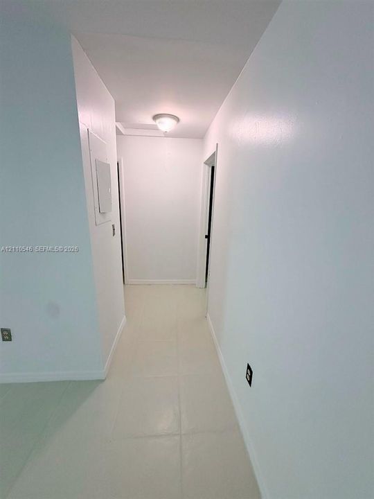 Hallway featuring neutral-toned tile flooring, smooth wall finishes, and a flush-mount ceiling light fixture