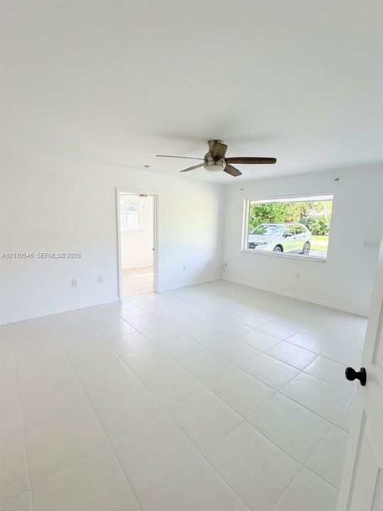 Interior space featuring white tile flooring, neutral walls, a central ceiling fan with integrated light fixture, and a large horizontal window