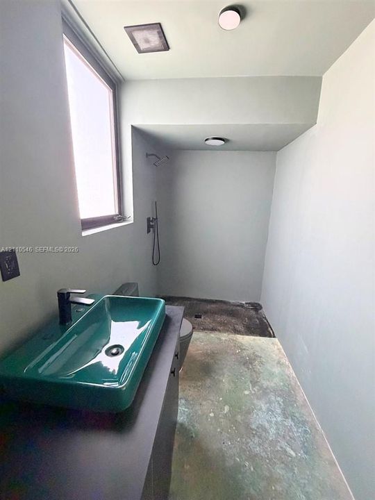 Green rectangular vessel sink, matte black faucet, dark-toned vanity, recessed ceiling lighting, and walk-in shower area