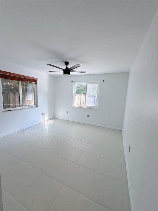Room featuring large-format neutral tile flooring, dual windows, and a matte black ceiling fan with integrated lighting