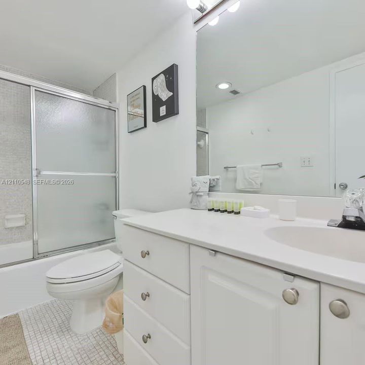 Bathroom featuring a white vanity with integrated basin, polished metal hardware, a wall-spanning mirror, frosted glass sliding shower enclosure, and mosaic floor tile