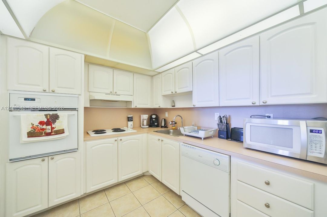 Kitchen featuring white cabinetry, integrated wall oven, white cooktop, tiled flooring, and recessed architectural lighting