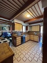 Kitchen featuring wood cabinetry, integrated built-in appliances, a tiled backsplash, exposed ceiling beams, and patterned tile flooring