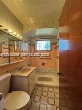 Bathroom featuring a vanity with an integrated basin, wall-mounted mirror cabinetry, and decorative tiled tub surround with an overhead shower fixture