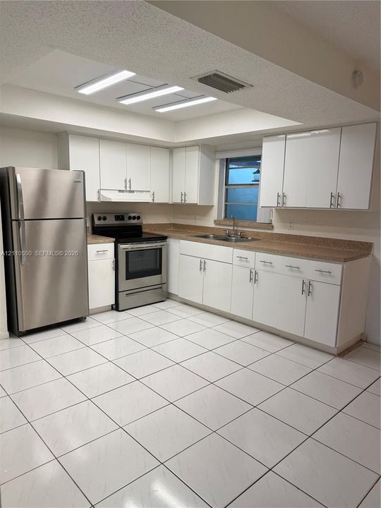 Kitchen featuring white flat-panel cabinetry, stainless steel appliances, recessed tray ceiling lighting, and tile flooring