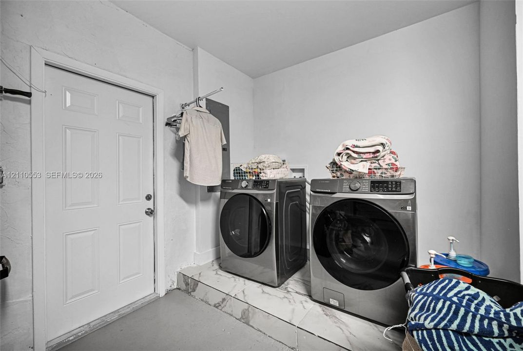 Laundry area featuring elevated tile flooring, white six-panel door, and integrated wall-mounted clothing rack