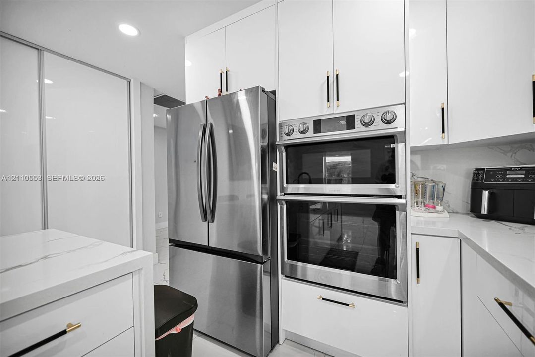 Kitchen featuring high-gloss white cabinetry, stone-finish countertops, stainless steel appliances, a double wall oven, and metallic hardware