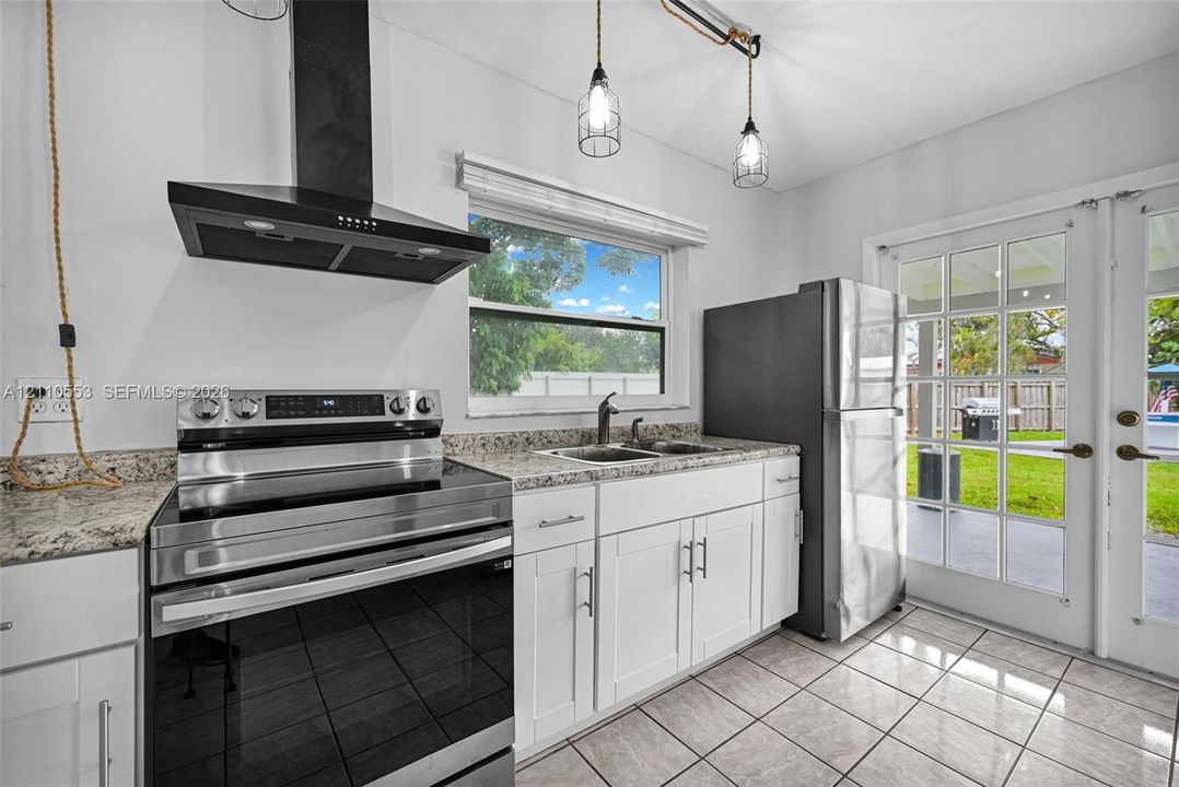 Kitchen featuring white cabinetry, stone-surface countertops, a stainless steel range, a black chimney-style range hood, and tile flooring