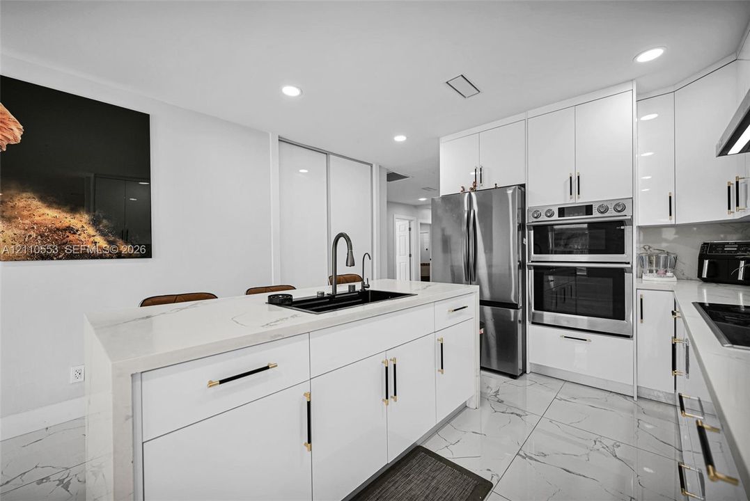 Kitchen featuring high-gloss white cabinetry, white stone-finish waterfall edge island, stainless steel double wall oven, integrated refrigerator, and large-format tile flooring