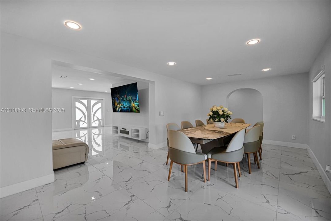 Polished stone-look flooring, recessed lighting, double entry doors with decorative glass inserts, and a distinct arched doorway
