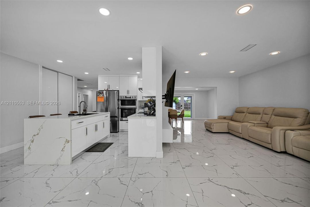 Kitchen area featuring an island with a waterfall countertop, white flat-panel cabinetry, recessed lighting, and large-format tile flooring
