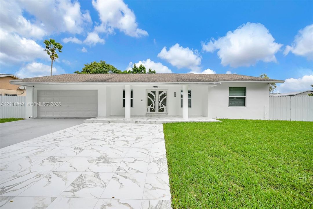 Single-story exterior featuring a stone-finish driveway, decorative glass double front doors, covered porch with structural columns, and solid fencing