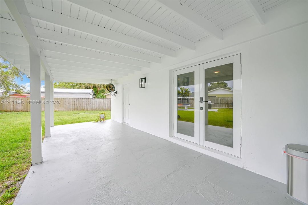 Covered patio featuring a painted concrete floor, white-finished exposed beam ceiling, full-glass French doors, and wall-mounted exterior lighting