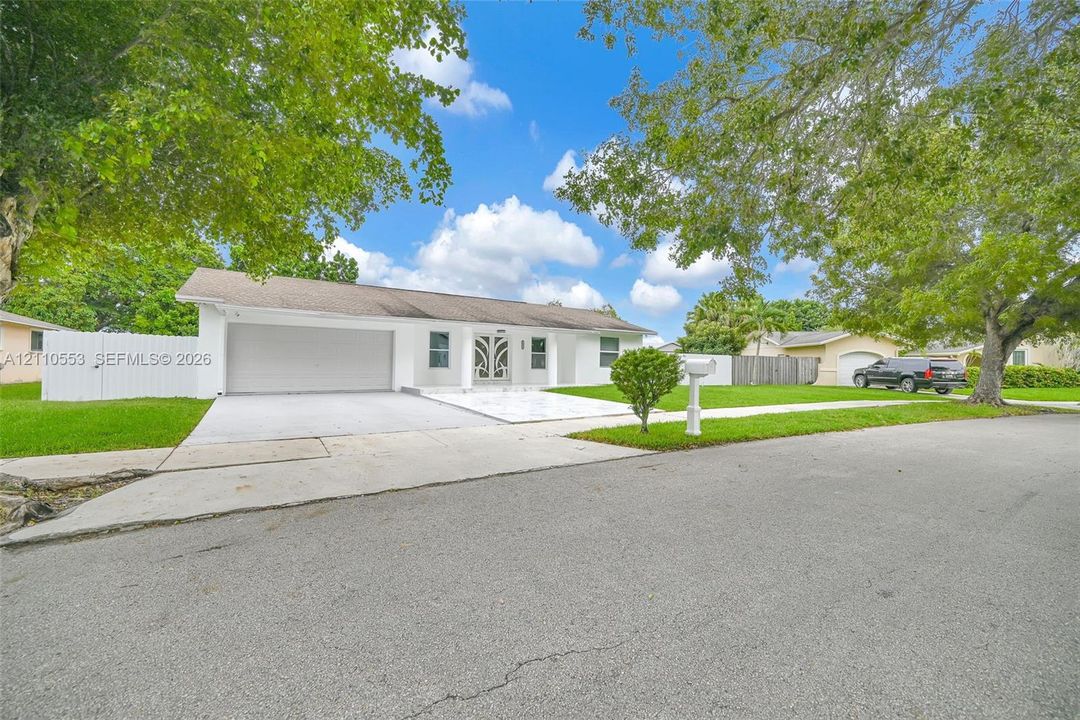 Single-story exterior featuring white stucco siding, a two-car garage, a decorative metal-frame front door, a concrete driveway, and white vinyl privacy fencing