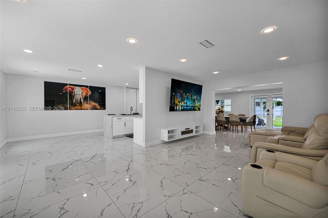 Large-format tile flooring with a neutral-veined pattern, recessed ceiling lighting, kitchen island with cabinetry, and double glass-paneled exterior doors