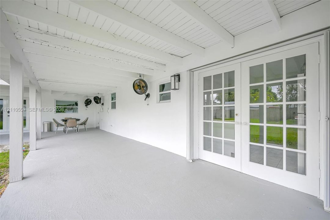 Covered patio featuring a painted wood-beam ceiling, glass-paned French doors, exterior wall-mounted lighting, and concrete flooring