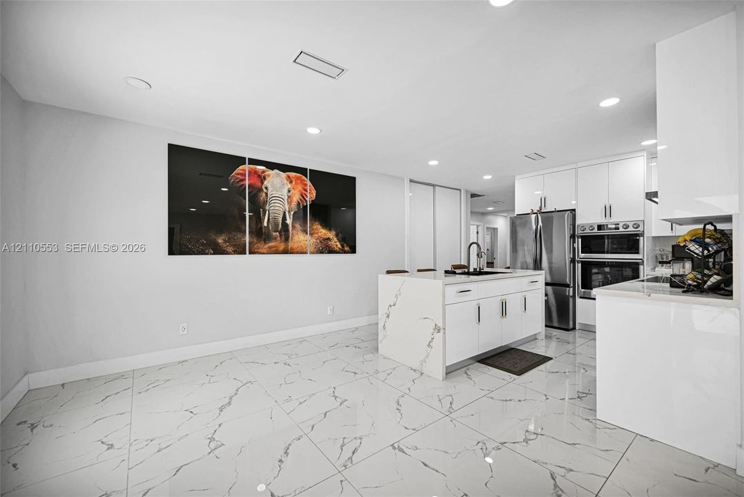 Kitchen featuring white high-gloss cabinetry, center island with stone-finish waterfall countertop, stainless steel double wall oven, and large-format porcelain tile flooring