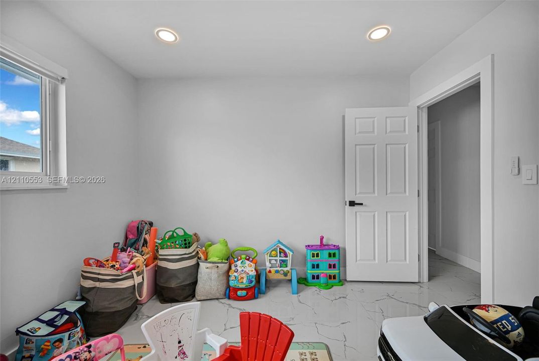 Interior room featuring white tile flooring with grey veining, neutral wall paint, recessed lighting, and a white interior door with matte black hardware